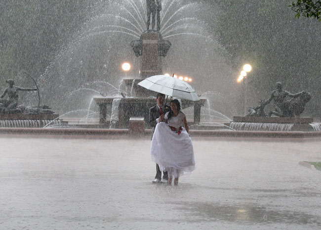 A recently married couple have their wedding photos taken in Hyde Park in torrential weather