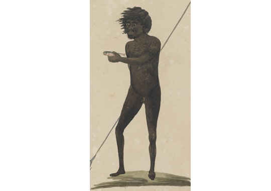 An Aboriginal man stands holding a five pronged spear and holding out a fish in his hand.
